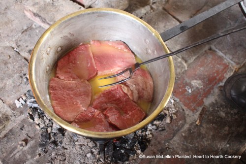 Cooking beef steaks at the hearth on a burner of embers.