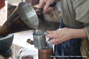 The second step in preparing a chocolate beverage from the receipt (recipe) To make Chocolate is to measure the heated water from the hearth.  I heated the water in a mulling cone and am using a tin cup to know how much water I am pouring in the chocolate pot so the proper amount of chocolate will be added.