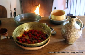 The table is set for the preparation of the 1744 receipt (recipe) Strawberry Cream.  Strawberries in the colander, cream in the salt glaze pitcher, pewter basin, and pewter bowl with sieve.