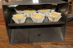 After the stoneware patty pans have been buttered and filled with the receipt (recipe) Cheese Loaves, the nine patty pans were set on a shelf of a tin baker.  The tin baker is set in front of the fire to be baked with reflective heat.  During baking, the patty pans were checked as not all receive the same degree of heat and some of the patty pans were moved to a different location on the shelf during baking.  Some were done before the rest.